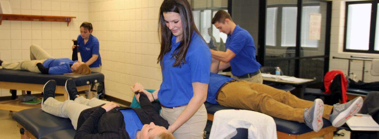 Physical Therapy student moving arm of a student who is lying on a table.