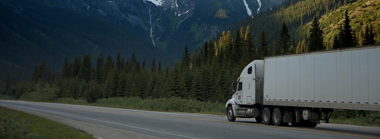 Semi truck traveling down the road with a mountain range in view.