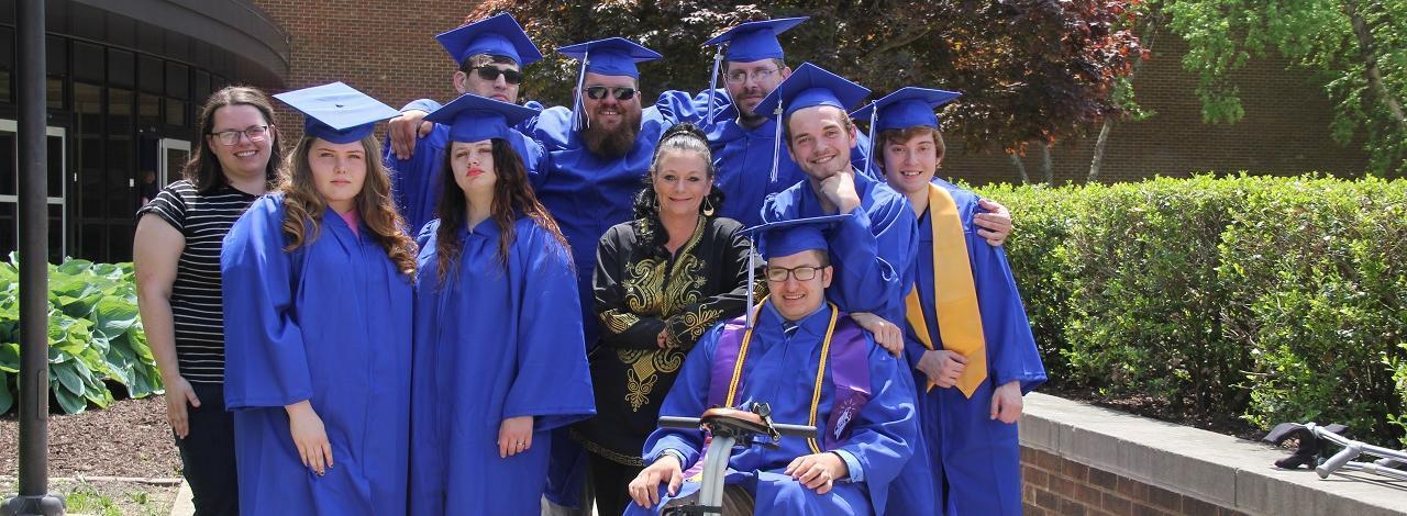 KC students in their graduation robes posing with faculty member Angenien Huffstutler.